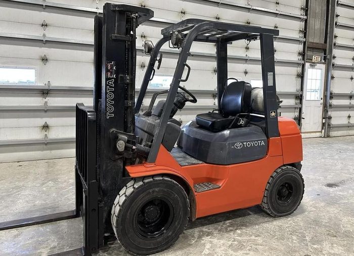 Toyota forklift, orange and black, parked in warehouse with metal door