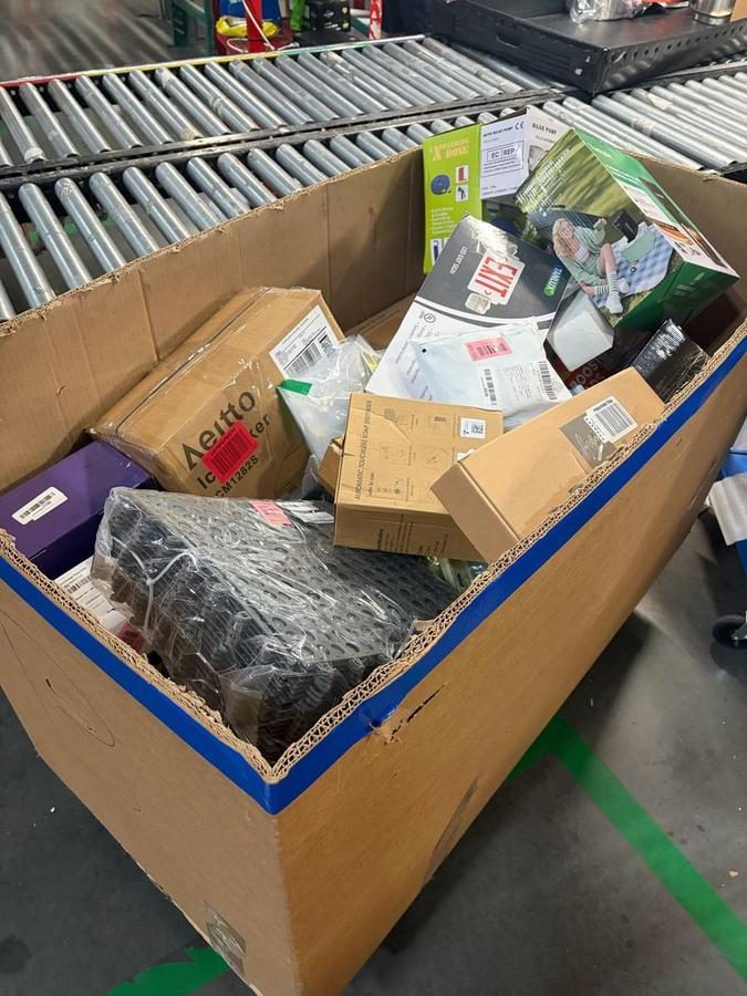 Large cardboard bin containing mixed merchandise and packaged items