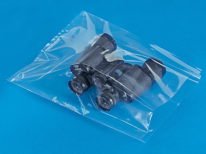 Night vision binoculars in clear protective plastic bag on blue surface