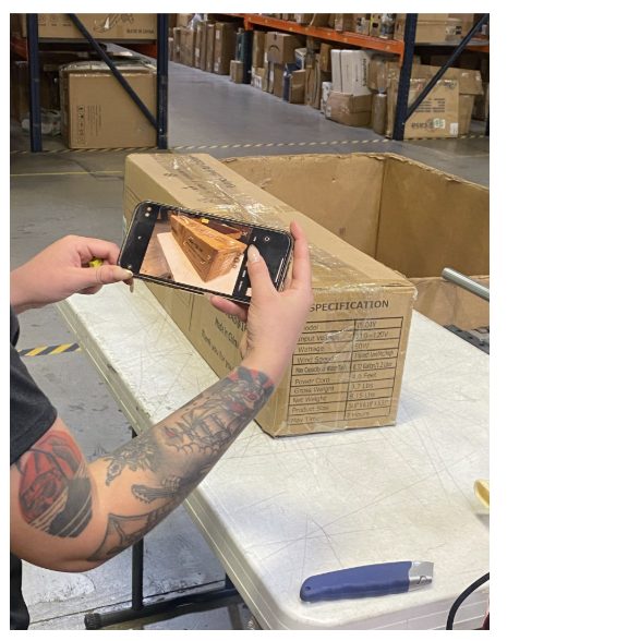 Worker photographing contents of cardboard box in warehouse