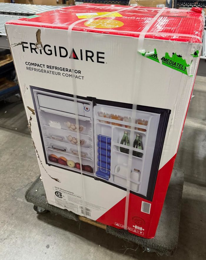 Frigidaire compact refrigerator in retail packaging on warehouse floor